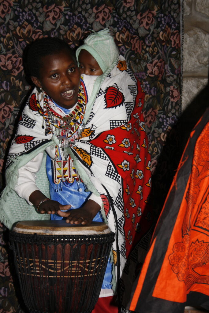 A Maasai mama plays the drum as others dance.